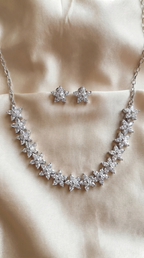 Silver rhodium-plated cubic zirconia floral necklace with matching star-cluster CZ stud earrings, displayed on ivory satin fabric.