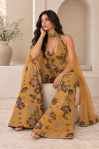 Seated model wearing the mustard embroidered halter top, palazzo trousers and sheer scarf.